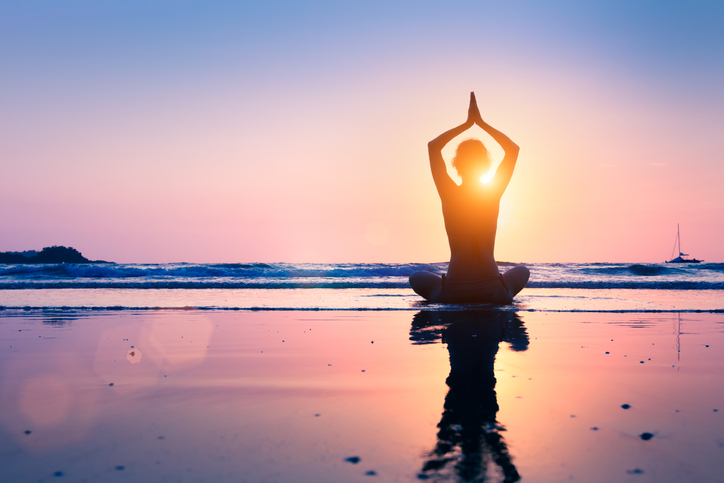 Silhouette of young woman practicing yoga, lotus position, and meditating on the beach